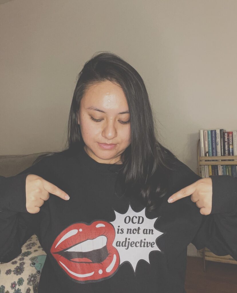 A photo of me pointing to my sweater, which reads ‘OCD Is Not an Adjective.