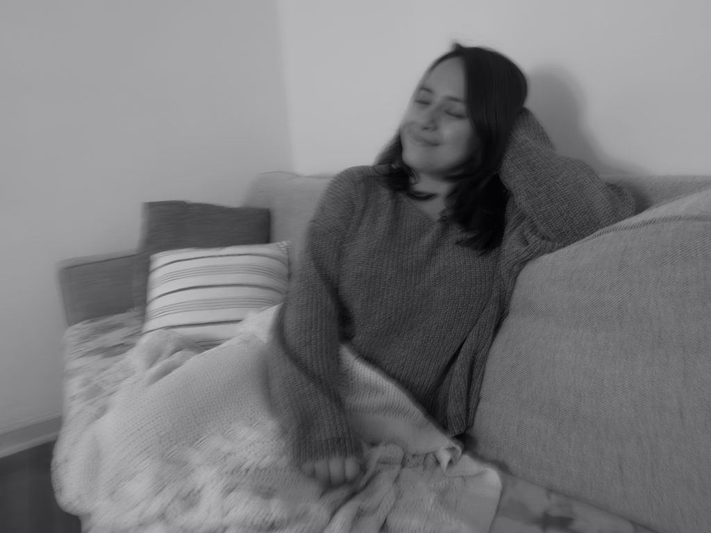 A black-and-white photo of me smiling peacefully with my eyes closed while sitting on my couch.
